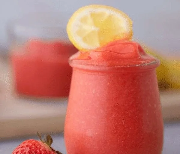 A refreshing frozen strawberry lemonade in a glass with strawberries and lemon slices.