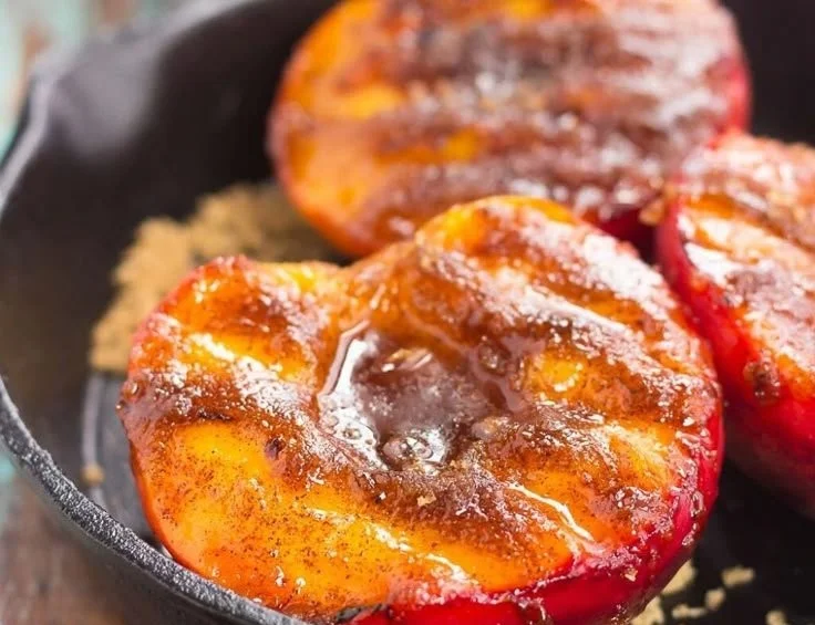 Grilled peaches sprinkled with cinnamon and brown sugar on a dessert plate.