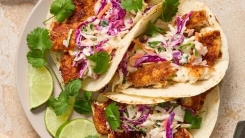 Cilantro-lime slaw fish tacos served with fresh toppings and lime wedges.