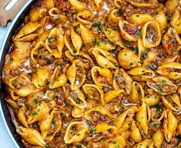 Creamy beef and shell pasta in a bowl garnished with parsley.