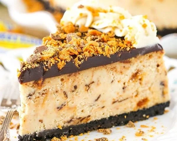 Creamy Butterfinger cheesecake topped with candy pieces and chocolate drizzle