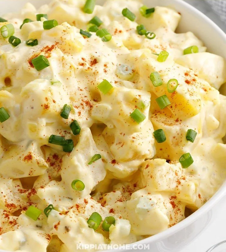 A bowl of creamy dill potato salad garnished with fresh dill and onions